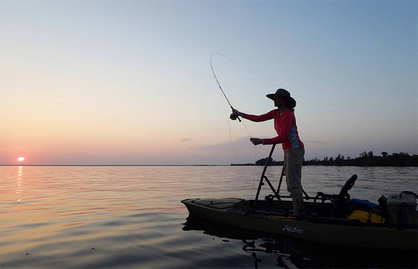 Silhouetted Lisa Ballard casts her fishing line from her kayak into Pine Island Sound at sunset.