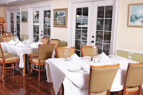 Antique wooden floors and set tables with beautiful white tablecloths and fine table settings: The Dining Room at The Tarpon Lodge