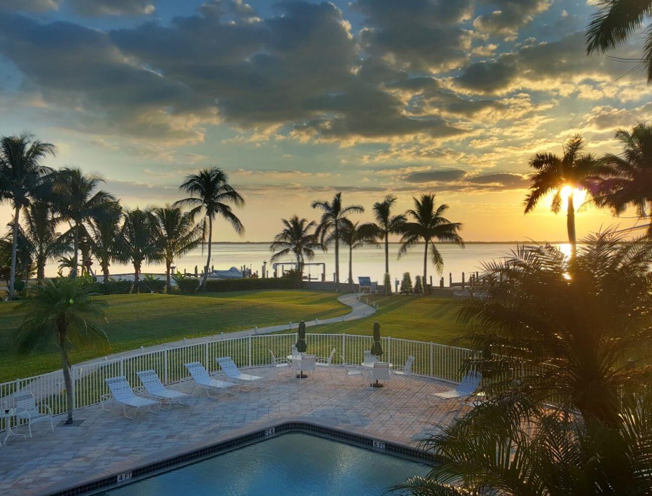 Balcony view of Tarpon Lodge overlooking the pool, the lawn, and the distant waterfront at sunset.